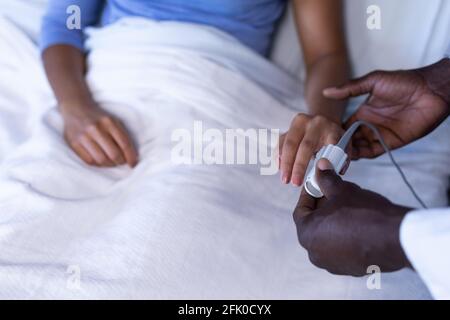 Midsection of african american male doctor putting oximeter on finger of patient in hospital bed Stock Photo