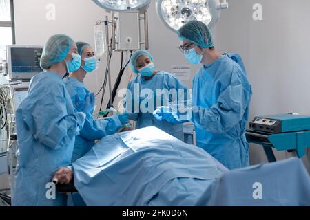 Diverse group of male and female surgeons in operating theatre wearing face masks performing surgery Stock Photo