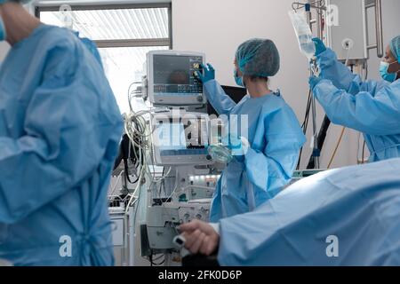 Caucasian female surgeon wearing face mask looking at monitor with patient lying in bed Stock Photo