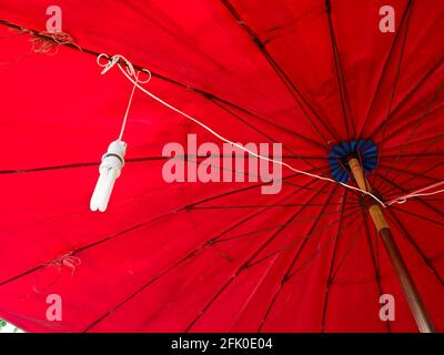 A compact fluorescent lamp hanging under a red umbrella Stock Photo