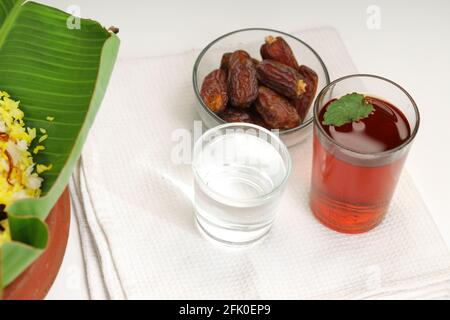 Dried dates,ramadan dried dates placed in a glass bowl with a glass of pure drinking water  and lime tea placed beside chicken biryani on a white text Stock Photo