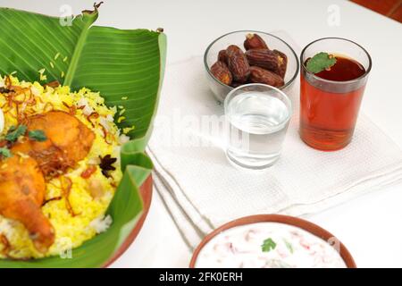 Dried dates,ramadan dried dates placed in a glass bowl with a glass of pure drinking water  and lime tea placed beside chicken biryani on a white text Stock Photo