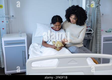 Mixed race mother comforting her sick daughter holding teddy bear in hospital bed Stock Photo
