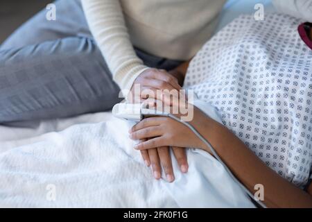 Midsection of mixed race mother comforting sick daughter in hospital bed with finger pulse oximeter Stock Photo