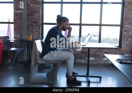 Thoughtful mixed race man sitting and using laptop in cafe Stock Photo