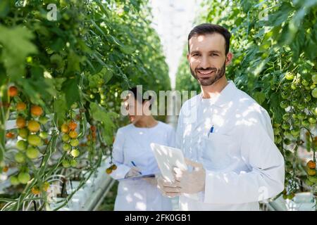 smiling quality inspector with digital tablet near african american colleague working on blurred background Stock Photo