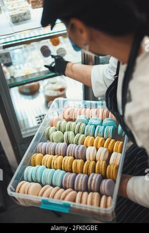 Woman in chef outfit putting fresh macarons on the shelf Stock Photo