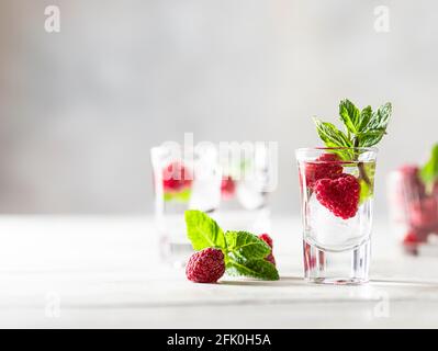 Raspberry vodka glass shot with fruit inside. Fresh summer shots for party. Berries in alcohol glass. Glass of sparkling water. Alcohol shots Stock Photo