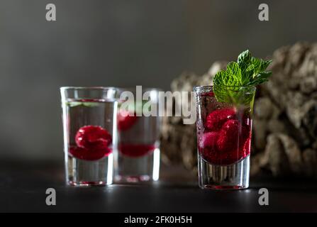 Raspberry vodka glass shot with fruit inside. Fresh summer shots for party. Berries in alcohol glass. Glass of sparkling water. Alcohol shots
