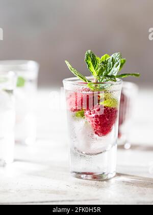 Raspberry vodka glass shot with fruit inside. Fresh summer shots for party. Berries in alcohol glass. Glass of sparkling water. Alcohol shots