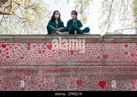 London, UK, 27 April 2021: Student doctors Charlie and Surina take a break sitting above the National Covid Memorial Wall as Prime Minister Boris Johnson still faces accusations of having preferred that 'bodies pile up' rather than have a third lockdown. With one heart drawn for each of the over 150,000 people who died in the UK coronavirus pandemic, the memorial stretches along the wall of St Thomas's Hospital, facing the Houses of Parliament on the opposite bank of the River Thames. Anna Watson/Alamy Live News Stock Photo