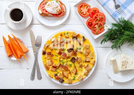 Poached egg sandwich, omelet with toasted bread slices, fresh vegetables, coffee on a white wooden table. Top view. Varieties of delicious, healthy br Stock Photo