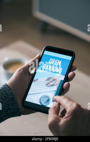 closeup of a young caucasian man, having a cup of coffee, watching at his smartphone, that reads the text open banking in its screen Stock Photo