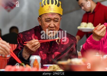 (210427) -- TAIYUAN, April 27, 2021 (Xinhua) -- Hu Zaizhong enjoys food at his birthday banquet at Xuejiawan Village, Liulin County, Lyuliang City of north China's Shanxi Province, on April 24, 2021. Hu Zaizhong, who has just turned 100, vividly remembers his wishes at different stages of his life: having decent food and clothing in his early days, teaching as many pupils as he could in his prime age, and enjoying quality time with his family for late years. Nonetheless, Hu made a new wish before blowing the candles on his birthday cake. All members of Hu's extended family flocked home on Apri Stock Photo