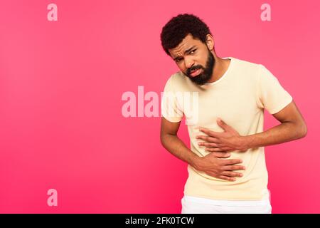 displeased african american man suffering from stomach ache isolated on pink Stock Photo