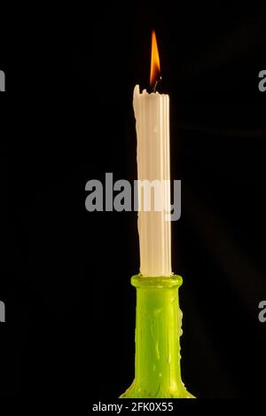 Single candle in green bottle on black background Stock Photo