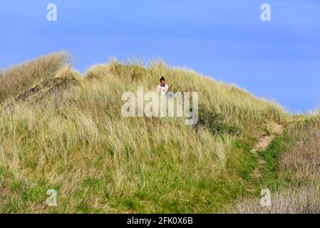 You're never alone with your phone. Woman sitting in sand dunes using her mobile phone. Stock Photo