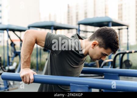 Young handsome man doing push-ups on the uneven bars outdoor. Sports, fitness, gymnastics workout. Stock Photo