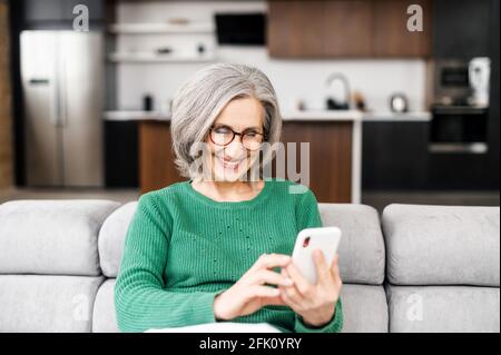 Contemporary senior woman spends time with a smartphone, mature woman scrolling news feed on the mobile phone, texting online with friends or children, enjoying messaging in social networks Stock Photo