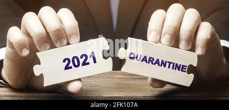 A man collects wooden puzzles with the words 2021 and Quarantine. Coronavirus pandemic infection COVID-19. Isolation of people. Obstruction of the spr Stock Photo