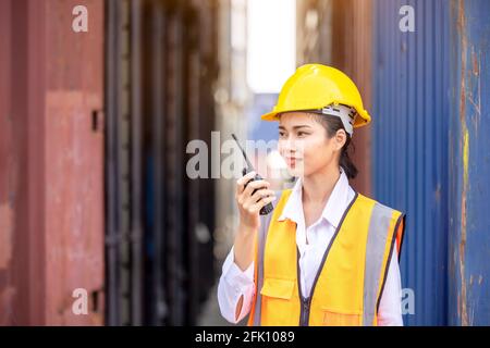 Portrait of Asian worker woman in safety uniform talking with walkie talkie to control work quality at container warehouse. working for logistic and s Stock Photo