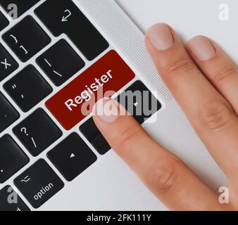 Person's fingers about to press "Register" key on a black laptop keyboard on an office desk. Click to register. Stock Photo