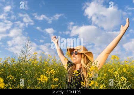 Happy woman enjoying summer raising arms in yellow flowers ,rapeseed field at sunset.Spring concept. Stock Photo