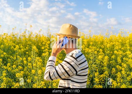 Unrecognizable man making a call on his phone outdoors in yellow flowers field. Stock Photo