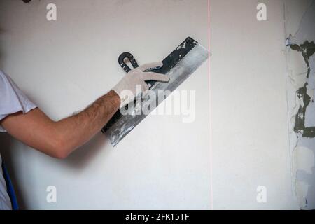 work on finishing the walls with mixtures of plaster and putty when building a house. builder worker plastering facade of high-rise building with putty knife. leveling stone walls Stock Photo