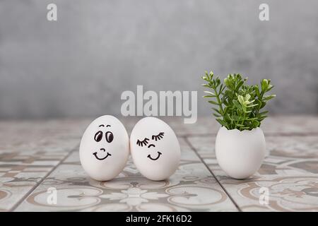 Easter composition. White eggs with funny faces painted on the table. A small bouquet in an egg. The minimal concept of Easter. An Easter card with a Stock Photo