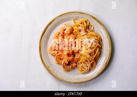 Tomato spaghetti pasta with shrimps prawns in sauce and parmesan cheese served in spotted ceramic plate over white marble background. Flat lay, copy s Stock Photo