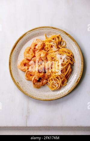 Tomato spaghetti pasta with shrimps prawns in sauce and parmesan cheese served in spotted ceramic plate over white marble background. Flat lay, copy s Stock Photo