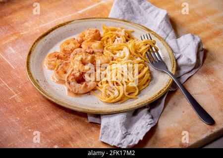 Tomato spaghetti pasta with shrimps prawns in sauce and parmesan cheese served in spotted ceramic plate with fork and cloth napkin over brown stone ba Stock Photo