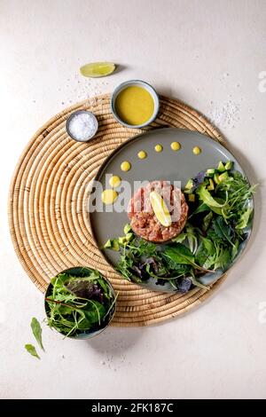 Tuna tartare with green salad, lime, avocado and mustard sauce serving on ceramic plate on straw napkin over white texture background. Flat lay, copy Stock Photo