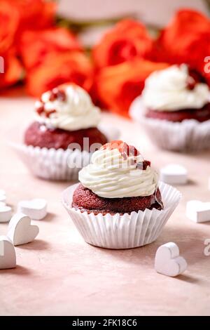 Homemade Red velvet cupcakes with whipped cream, white napkin with ribbon, roses flowers, wooden hearts over pink texture background. Valentines day d Stock Photo