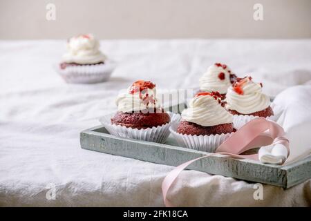 Homemade Red velvet cupcakes with whipped cream on wooden tray, white napkin with ribbon on white linen table cloth. Stock Photo