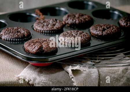 Fresh baked homemade chocolate cupcakes muffins in form for cooking standing on kitchen table with tablecloth. Home bakery Stock Photo