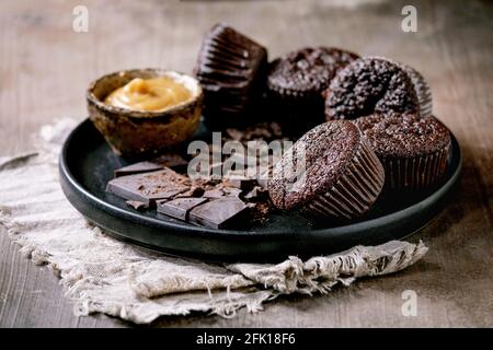 Homemade chocolate cupcakes muffins with salted caramel sauce and chopped dark chocolate on black ceramic plate over concrete texture background. Stock Photo