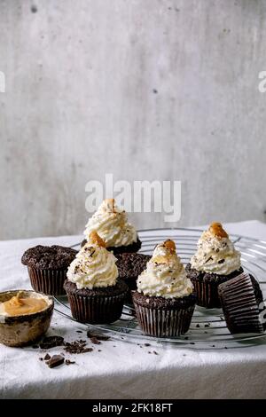 Homemade chocolate cupcakes muffins with white whipped butter cream and salted caramel, served with chopped dark chocolate on cooling rack on white ta Stock Photo