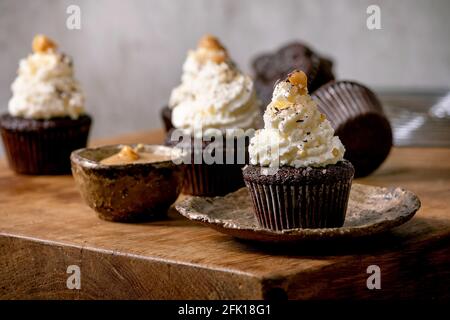 Homemade chocolate cupcakes muffins with white whipped butter cream and salted caramel on ceramic plate on wooden table. Stock Photo
