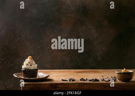 Homemade chocolate cupcakes muffins with white whipped butter cream and salted caramel on ceramic plate, served with chopped dark chocolate on wooden Stock Photo
