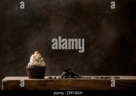 Homemade chocolate cupcakes muffins with white whipped butter cream and salted caramel on ceramic plate, served with chopped dark chocolate on wooden Stock Photo
