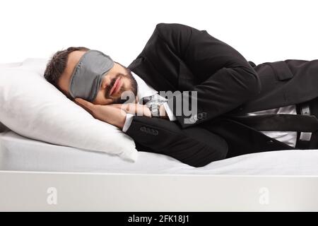 Businessman in a suit and tie sleeping on a bed and wearing a sleep mask isolated on white background Stock Photo