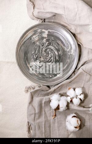 Empty grey ceramic plate japanese Nerikomi technique with cotton flowers over white linen tablecloth. Table setting. Flat lay, space. Stock Photo