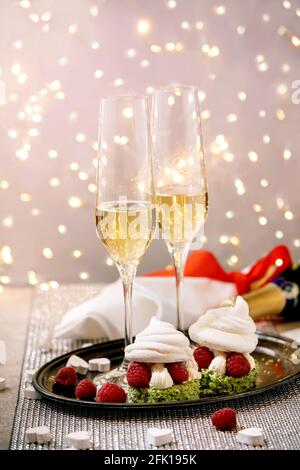 St. Valentine festive table setting with two Champagne glasses and berry meringue desserts on tray standing on silver sparkling table, white hearts, b Stock Photo