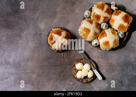 Homemade Easter traditional hot cross buns on ceramic plate with butter, jug of milk, quail eggs over brown texture background. Flat lay, space Stock Photo