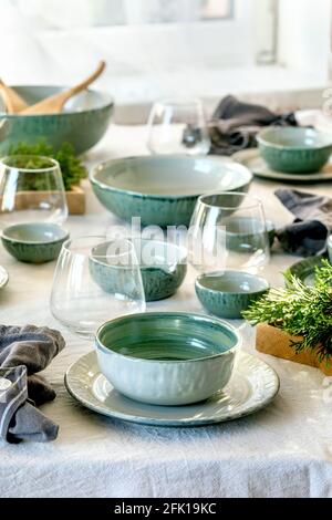 Rustic Christmas table setting with empty craft ceramic tableware, plates and bowls, xmas angel decorations, glasses, green branches on white tableclo Stock Photo
