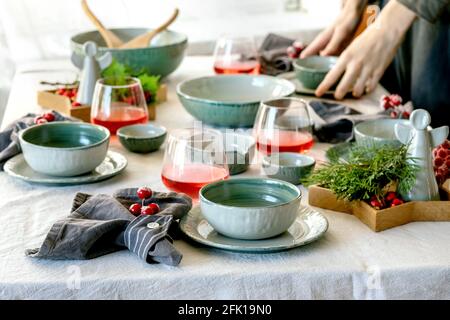 Rustic Christmas table setting with empty craft ceramic tableware, plates and bowls, xmas angel decorations, glasses of red juice, green branches and Stock Photo