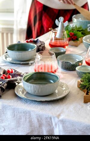 Rustic Christmas table setting with empty craft ceramic tableware, plates and bowls, xmas angel decorations on white tablecloth in front of the window Stock Photo