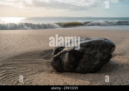 PANAMá, PANAMA - Apr 25, 2021: Rock laying on the sand of a beach on a sunset, waves hitting the beach on the blue sky Stock Photo